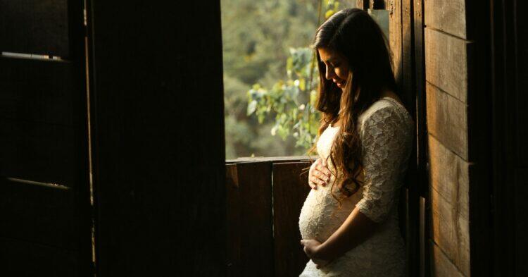 Pregnant woman standing by window (Unsplash | Mel Elias)