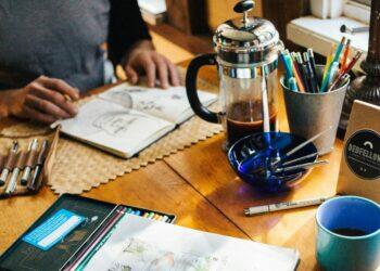 Desk with scattered drawing supplies and coffee (Unsplash | Rachael Gorjestani)