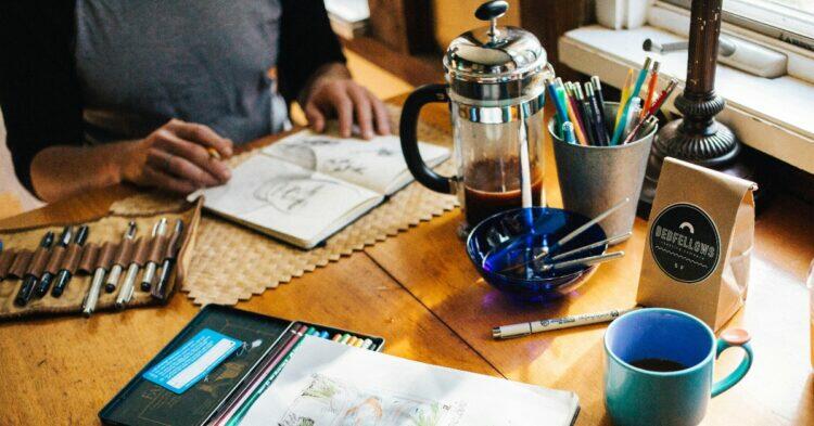 Desk with scattered drawing supplies and coffee (Unsplash | Rachael Gorjestani)