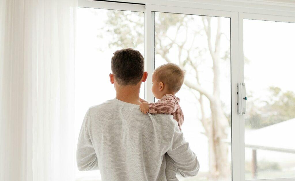 Father holding son and standing in front of window (Unsplash | Kelli McClintock)