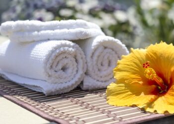 White towels sit on a bamboo mat next to a yellow hibiscus flower.