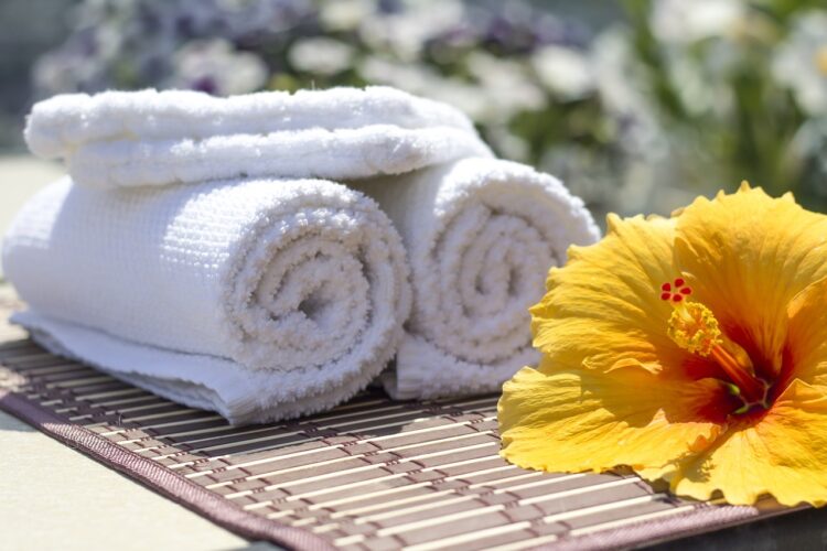 White towels sit on a bamboo mat next to a yellow hibiscus flower.