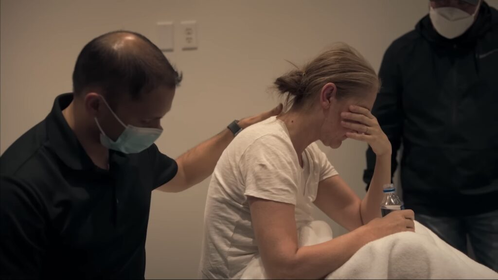 A screenshot of singer Celine Dion being comforted by a man in a mask from the documentary “I Am: Celine”