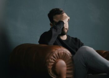 a man holds his head while sitting on a sofa