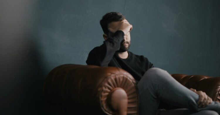 a man holds his head while sitting on a sofa