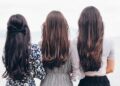 three woman looking back and facing body of water
