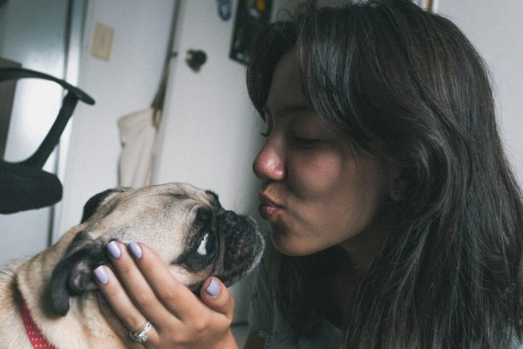 A woman with long dark hair about to kiss a pug dog