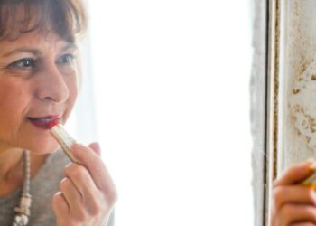 Photo of Older Woman Applying Lipstick In Front of the Mirror