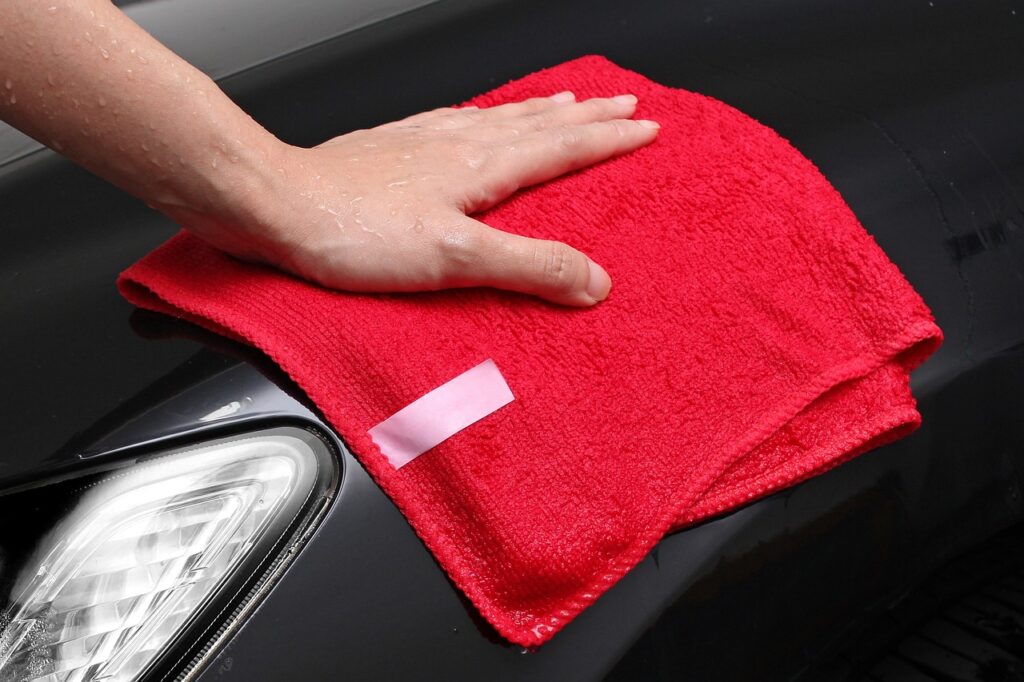 Someone using a red microfiber towel to wash a black car