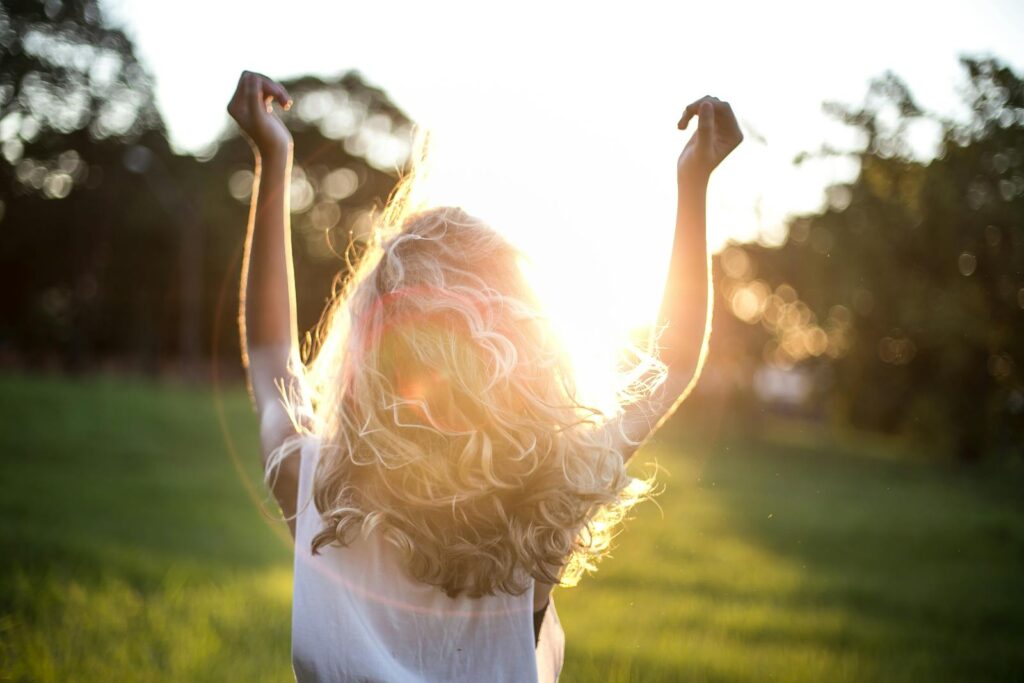 Woman Wearing White Top holds her arms up in the sun