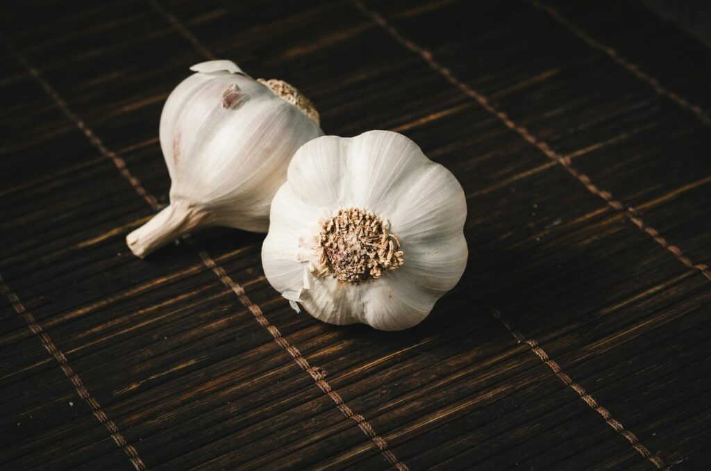 Two whole white garlic vegetables on a dark bamboo mat