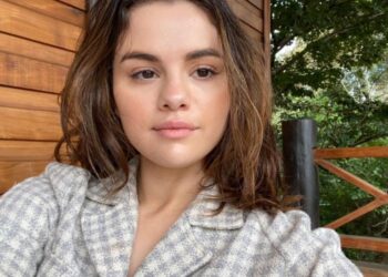 Selena Gomez taking a selfie, while sitting on a deck at a cottage.