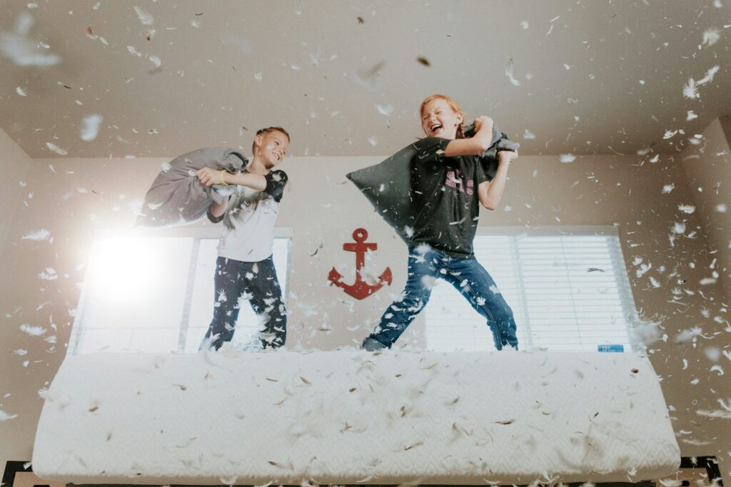 two toddlers pillow fighting on a white bed