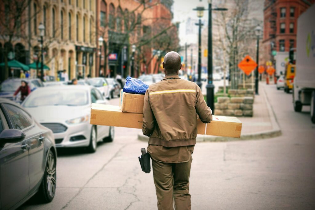 man in brown jacket beside car delivering a package