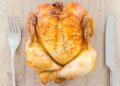 roasted chicken on a wooden block next to knife and fork