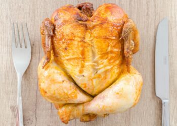 roasted chicken on a wooden block next to knife and fork