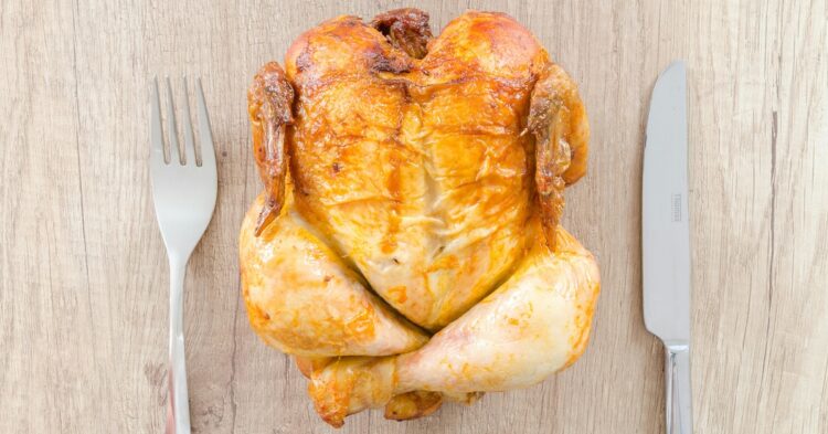 roasted chicken on a wooden block next to knife and fork
