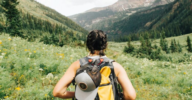 person carrying yellow and black backpack walking between green plants