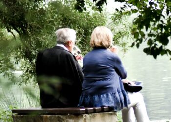 two people sitting on pavement facing on body of water