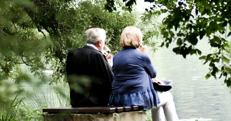 two people sitting on pavement facing on body of water