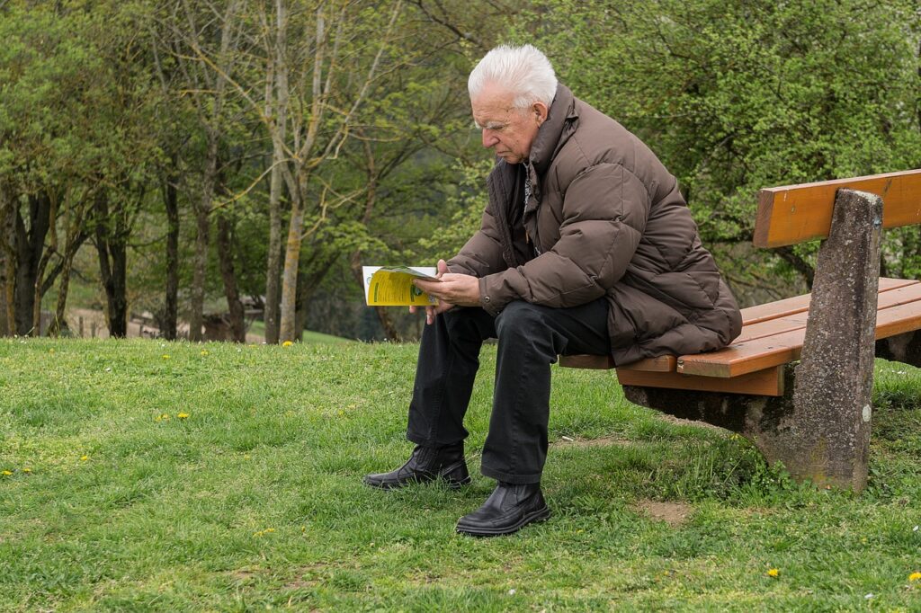an older man sitting on a park bench looking at a book