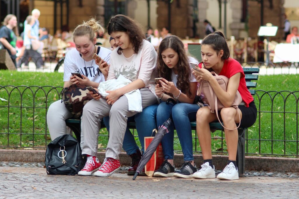 girls sitting on a bench using cell phones