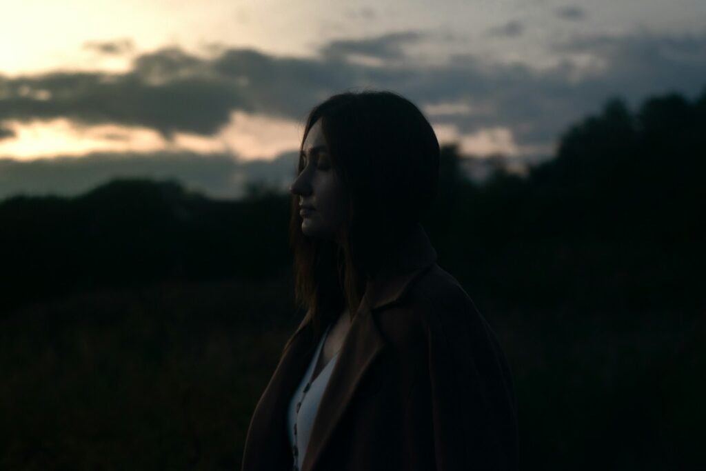 a woman standing in a field at sunset