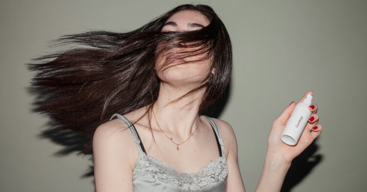woman holding a spray bottle with flowing hair in the air