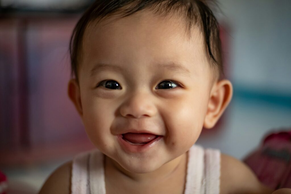 a smiling baby with dark hair in white tank top