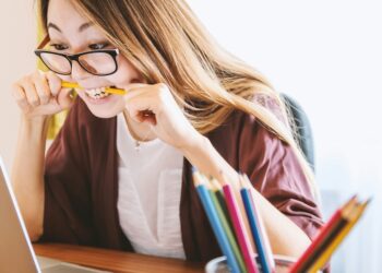 woman starring at a laptop screen biting a pencil