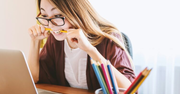 woman starring at a laptop screen biting a pencil