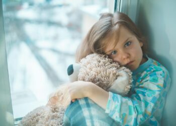 girl in blue white and red plaid shirt hugging brown teddy bear