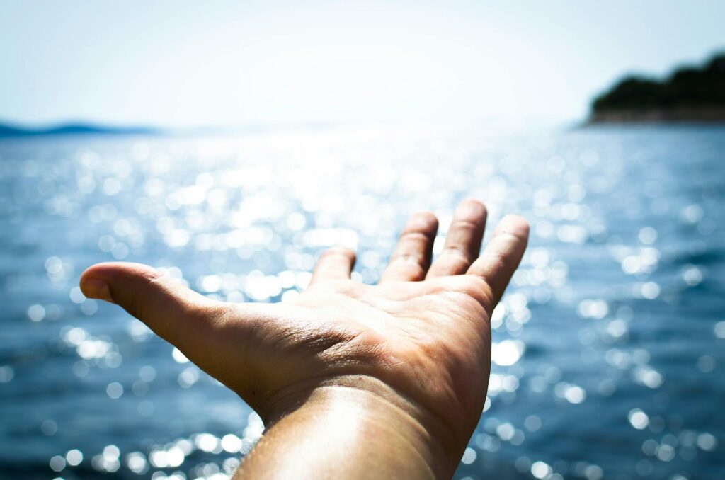 Person Hand Reaching Body of Water