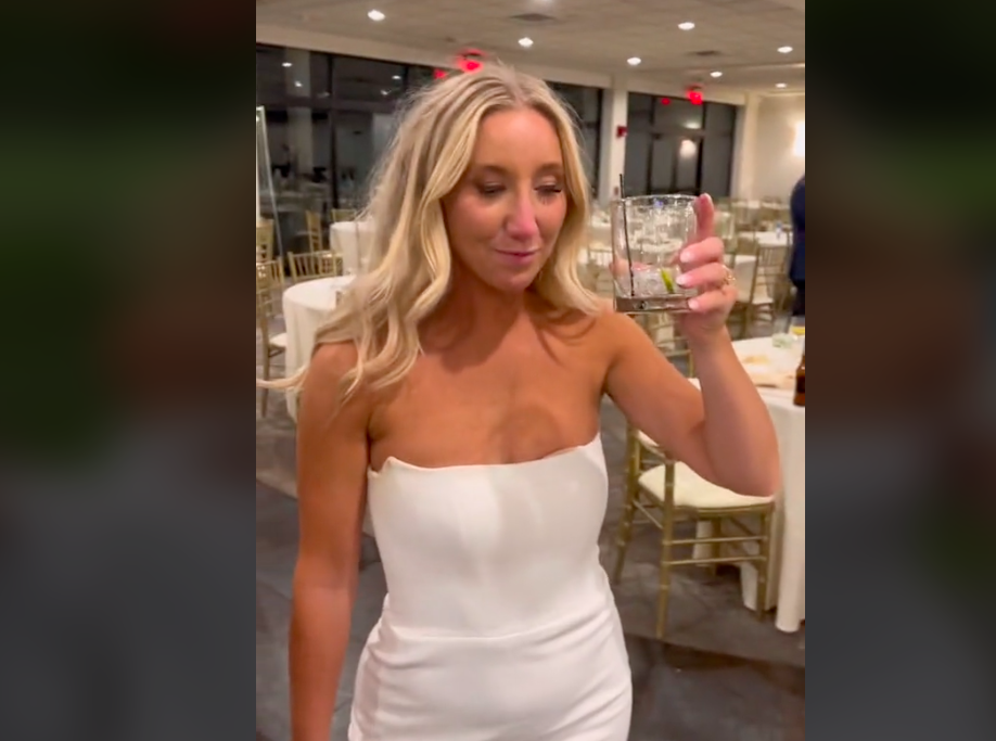 Blond woman in a wedding dress holds up a cocktail glass