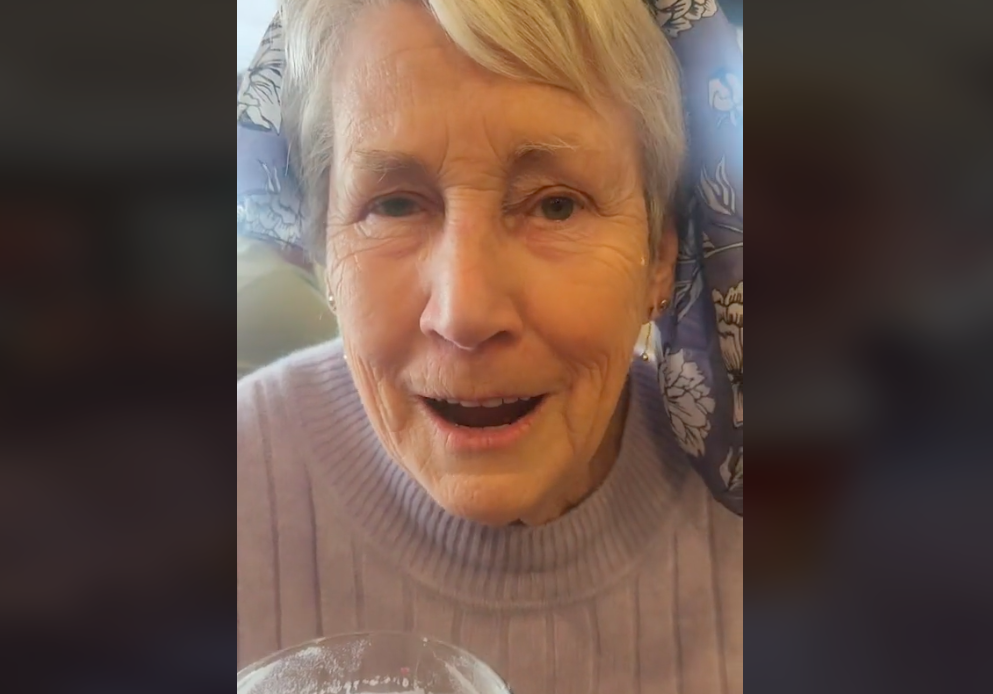 An older woman in a purple sweater smiles at the camera