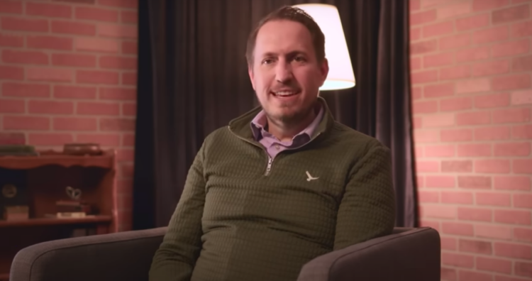 Travis Shreeve in a green sweater sits in front of a background during an interview