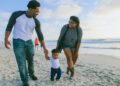man in black and white striped long sleeve shirt holding baby in white shirt on beach