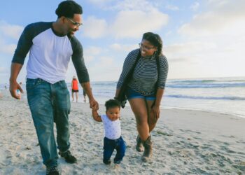 man in black and white striped long sleeve shirt holding baby in white shirt on beach