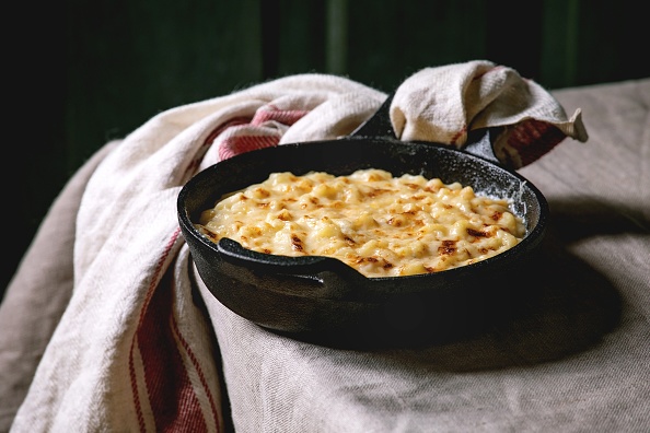 Classic american dish baked mac and cheese in cast iron pan with towel on kitchen table with linen tablecloth
