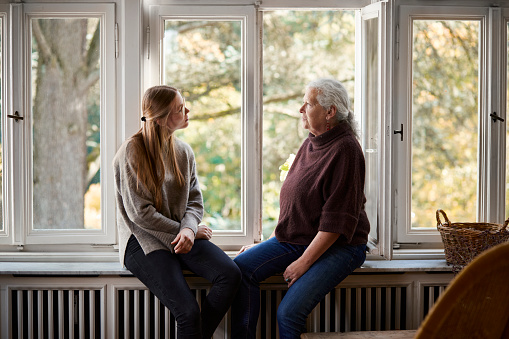 Grandmother and adult granddaughter sitting on windowsill