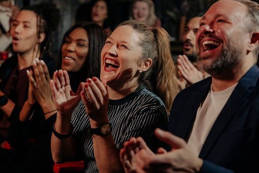Multiracial audience laughing and applauding while watching comedy stage show in theater