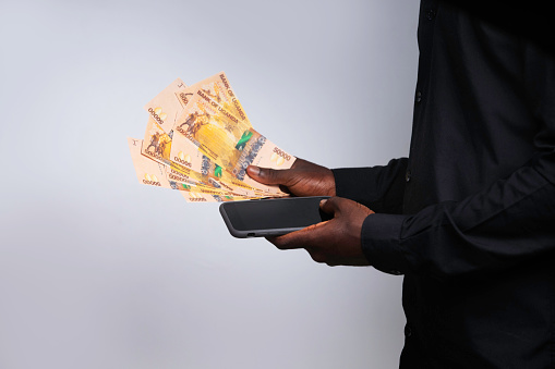 black African male person Hand Holding mobile phone and Ugandan shilling notes, winning, receiving, getting, transferring money, long sleeves shirt
