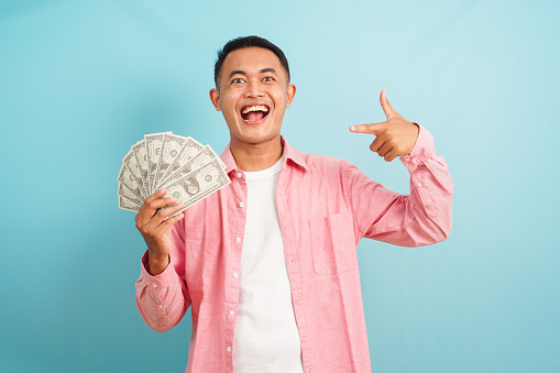 Smiling man pointing to fan of money dollar on blue background
