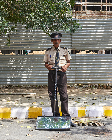 Security guard with mirror to detect bombs underneath cars