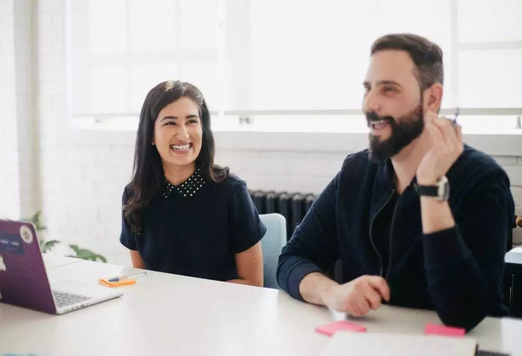 Two people smiling in work office (Unsplash | Jason Goodman)
