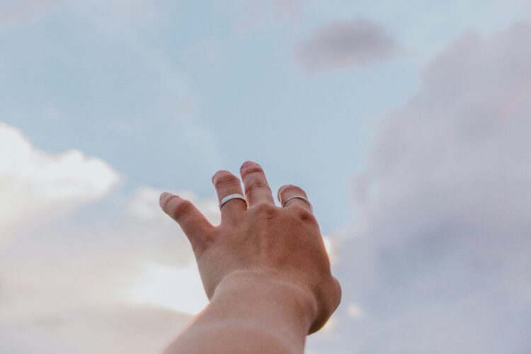 hand reaching out to the clouds in the sky