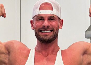 Bodybuilder Joey Swoll posing in a gym, showcasing his muscular physique with gym equipment