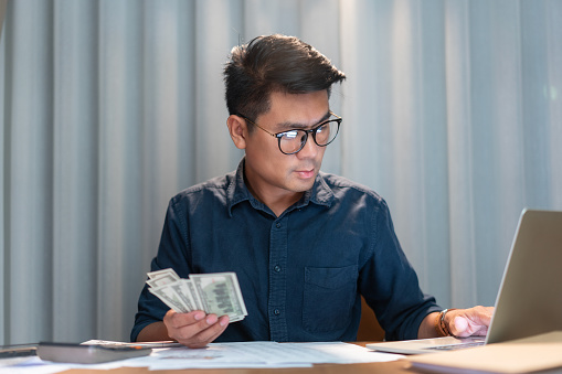 Businessman Handling Cash While Working on Laptop