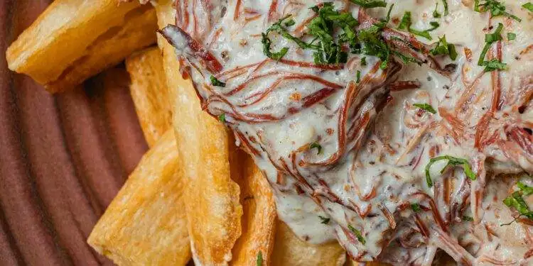 Close-up of Brazilian carne de sol with creamy sauce served on crispy cassava fries. A Maceió culinary delight.
