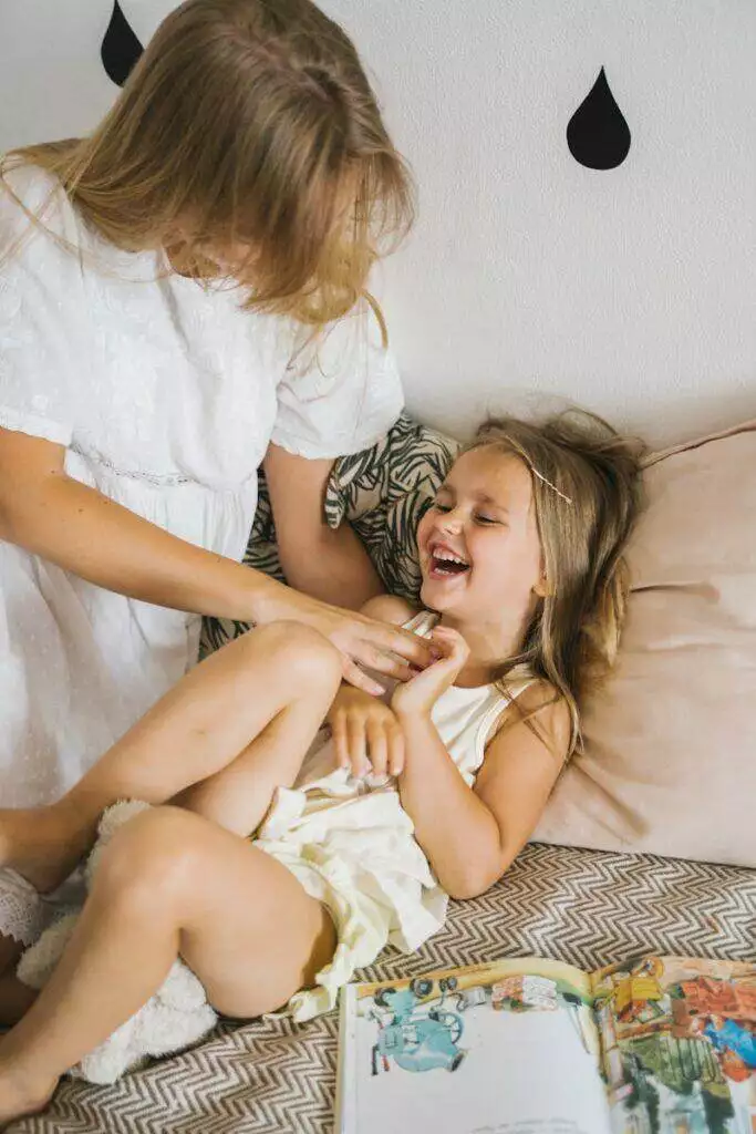 A mother tickling her laughing daughter, sharing a fun and loving moment indoors.